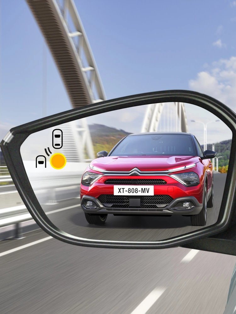 Dodehoekwaarschuwing in de spiegel van de Citroën ë‑C4 X die een naderend voertuig van achteren toont.